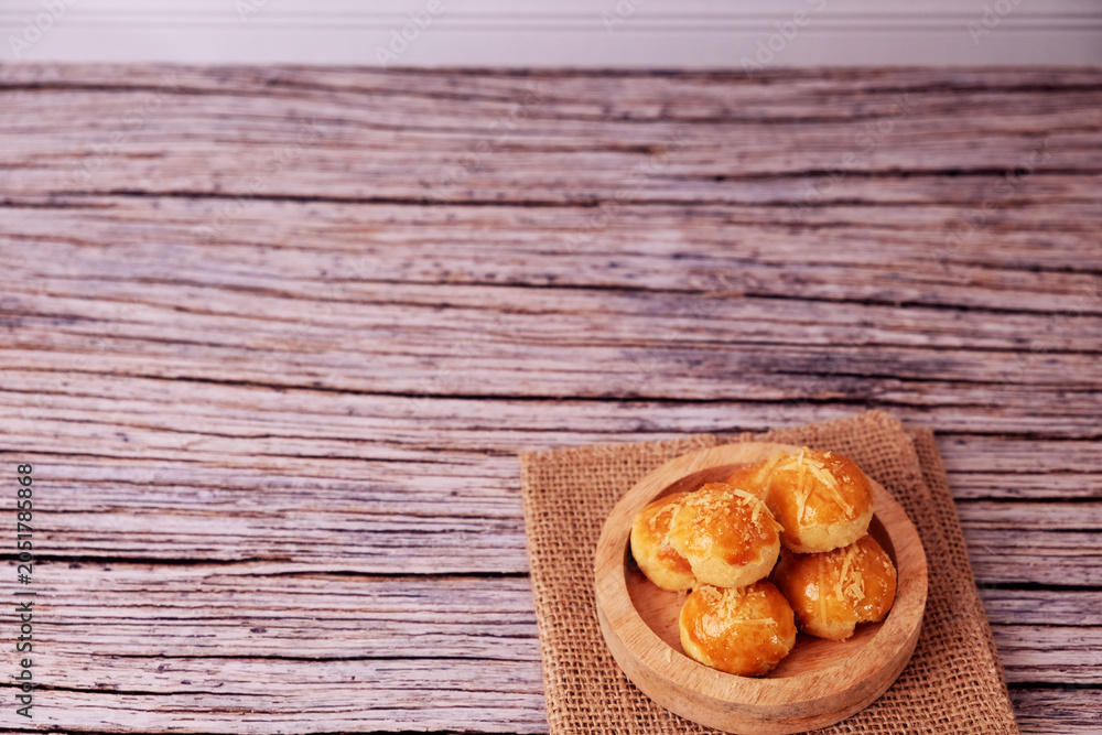 Fototapeta premium Kue Nastar or Golden pastries rest in a wooden bowl. Bowl sits atop burlap on aged wood. Warm tones evoke comfort and homemade charm. Ideal for food blogs, bakery ads, or cozy lifestyle content