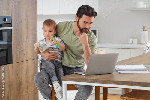 Cuadro en lienzo Father working with laptop and his little baby at table during parental leave in