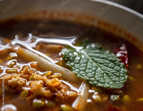Ultra-close macro shot of authentic spicy Penang Assam Laksa featuring glossy tamarind soup base fresh mint leaf and bean sprouts in a white bowl