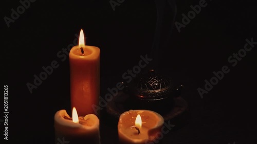 Three magic Christmas wax candle flames calm burning in home in white smoke from incense aroma stick on black dark background with copy space. Closeup yoga, spa, wellness, relaxation. No people