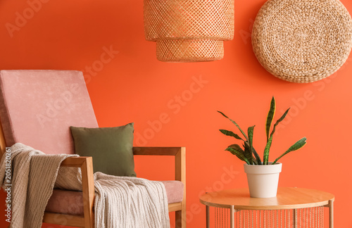 Foto Armchair and houseplant on table near orange wall in room, closeup