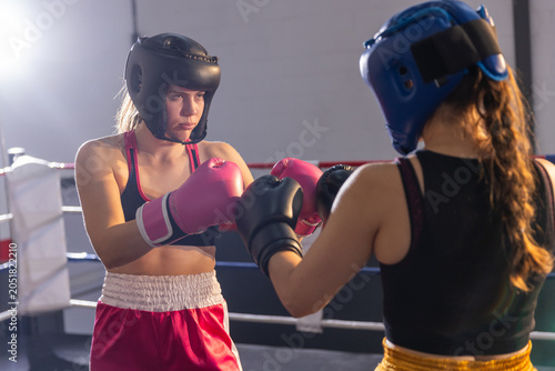 Foto Two female boxers sparring in gym ring, wearing headgear, sports tops, pink and