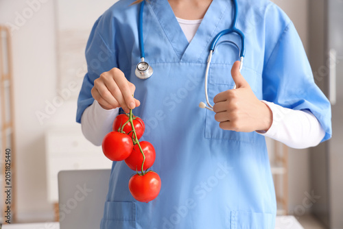Female nutritionist with tomatoes showing thumb-up in office, closeup