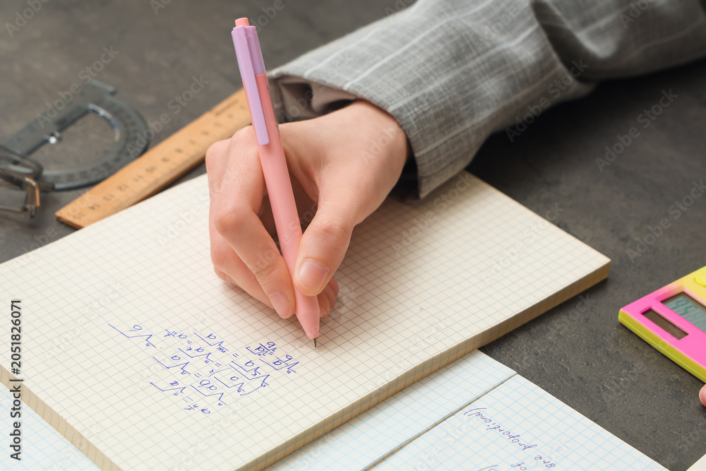 Naklejka premium Woman writing math formulas in notebook at dark table, closeup