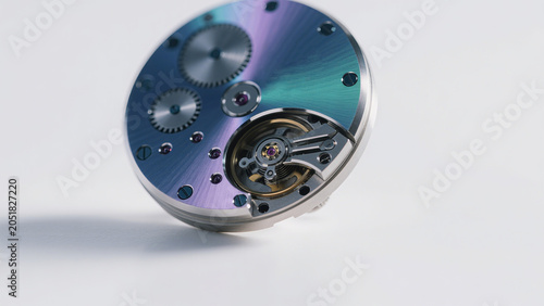 Luxury watch movement with iridescent blue-purple finish, precision mechanical horology parts on clean white background