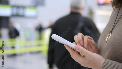 Person holds phone in busy airport terminal. Focus on hands and device. Background shows travelers and green barriers. Scene shows modern travel and digital connectivity. Ideal for travel, tech