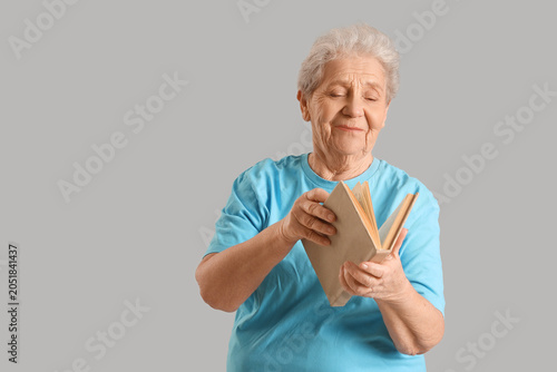 Senior woman reading book on grey background