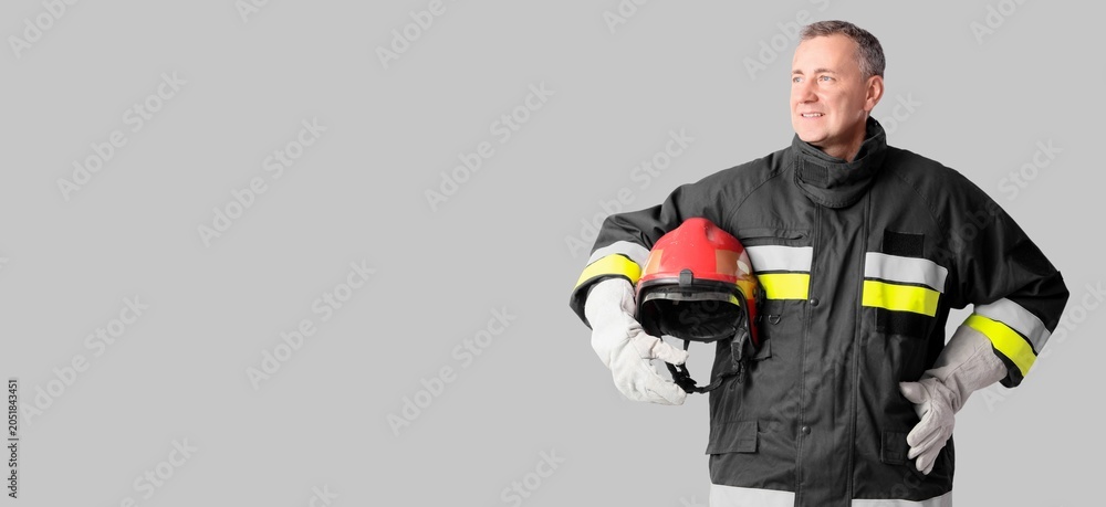 Fototapeta premium Smiling firefighter in protective gear holding red helmet, safety and emergency services professional, isolated on gray background