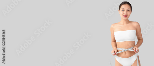 Fotografija Young Asian woman in underwear measuring waist on light background