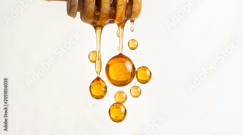 Pure golden honey dripping with flowing balls and droplets from wooden dipper