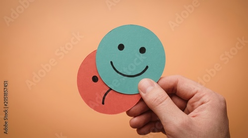 Hand holding smiling and frowning paper faces on orange background
