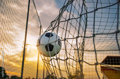 Soccer ball entering the goal net , amazing sunset in background 