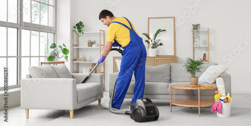 Janitor vacuuming sofa in room