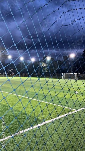 Mini football field with artificial green grass at night under stadium lights behind safety net