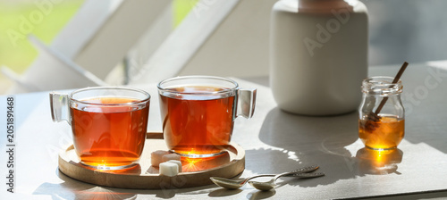 Foto Two glass cups of hot black tea with sugar cubes and honey jar on wooden tray, m