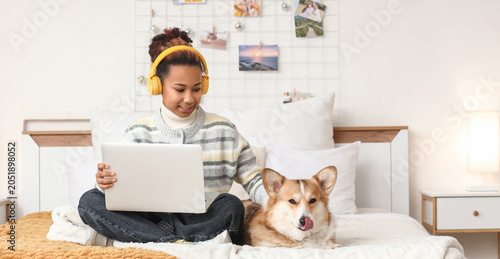 Teenage African-American girl with laptop and Corgi dog in bedroom