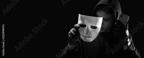 Konstfotografi Cybercrime and online fraud with hacker in hoodie holding mask and smartphone in