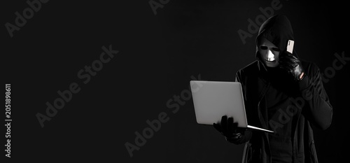 Quadro su tela Cybercrime and data theft: anonymous hacker in mask and hoody using laptop and s