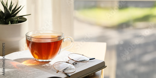 Foto Cozy home reading scene with hot tea, open book, and eyeglasses by sunny window