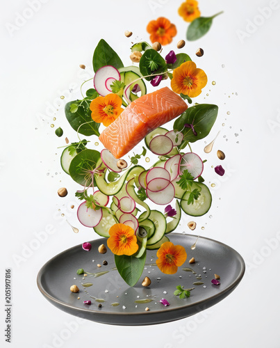 Fresh salmon fillet floating above a plate with sliced vegetables and edible flowers