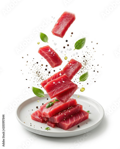 Fresh raw tuna fish slices falling onto a ceramic plate with basil leaves and peppercorns