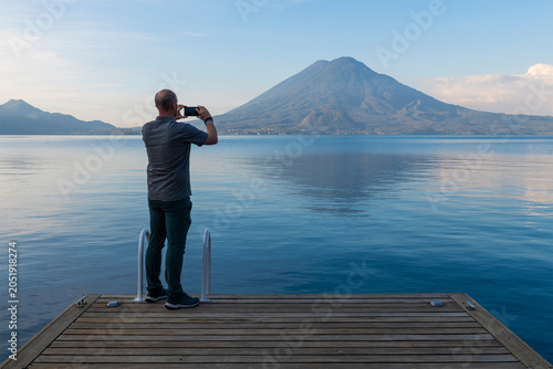 Obraz na płótnie Tourist taking photographs with smartphone of Atitlan Lake with Toliman and Atitlan Volcano, Guatemala