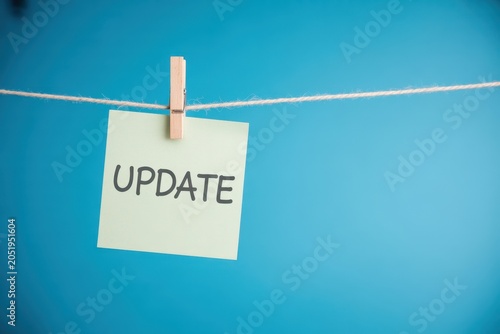 Green sticky note with word UPDATE hanging on a string with a clothespin on blue background
