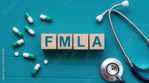 FMLA acronym made of wooden blocks with pills and stethoscope on teal background