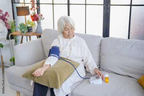 Old senior asian woman  blood pressure in house healthcare with pump for wellness