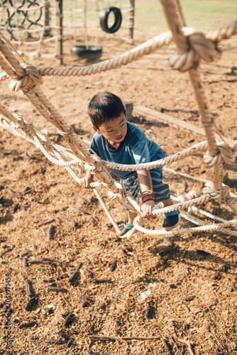 Asian child climbing a rope playground net outdoors in natural sunlight. Concept of adventure, physical development, balance, coordination, confidence, active play, and childhood exploration.