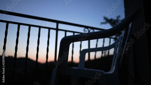 A solitary white plastic chair sitting on a balcony at twilight.