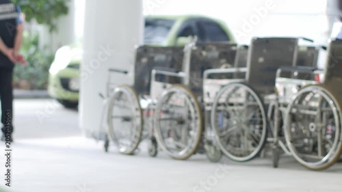 Row of hospital wheelchairs parked outside medical facility entrance with security guard in healthcare service