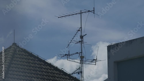 Old rooftop television antenna with multiple elements against clear blue sky and white clouds urban residential communication