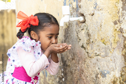 Young Indian thirsty girl child drinking fresh clean water from tap in hot summer. concept of hydration, South Asia water crisis Rural india life.