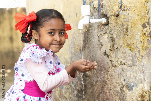 Smiling Indian girl child drinking fresh clean water from tap looking at camera. concept of hydration, South Asia water crisis Rural india life.