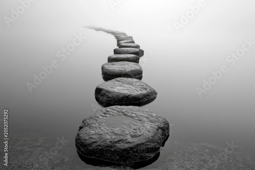 Stepping stones leading into dense fog across a calm lake in a minimalist black and white composition for wellness and spiritual marketing