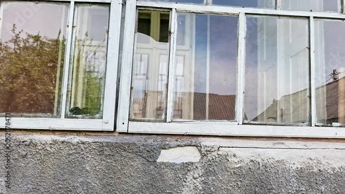 Exterior view of an old building window with weathered frames and reflective glass panes. Rural architecture scene showing age, wear, residential character, and everyday surroundings