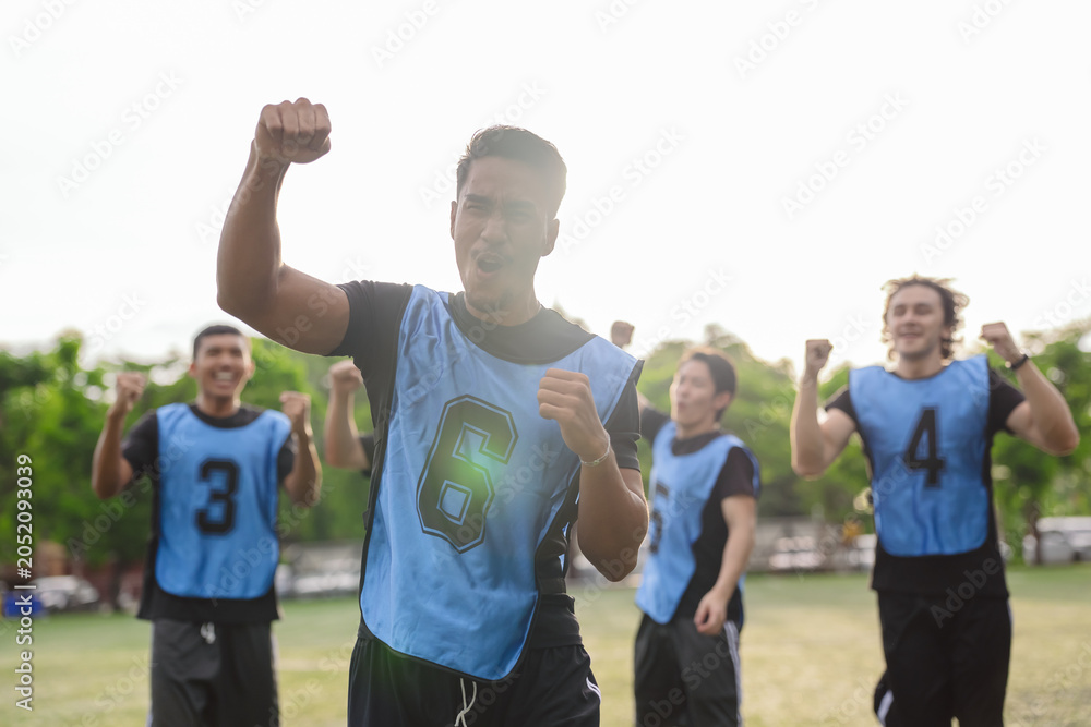 Obraz premium Excited soccer player raising fist and shouting to celebrate victory. Teamwork, success, and active lifestyle concept during a sports match on an outdoor field.