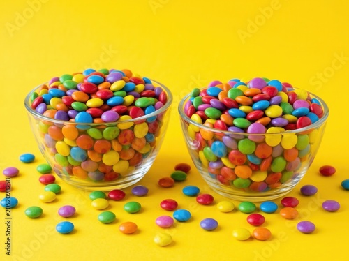 Two Glass Bowls Filled with Colorful Chocolate Candies on a Bright Yellow Background