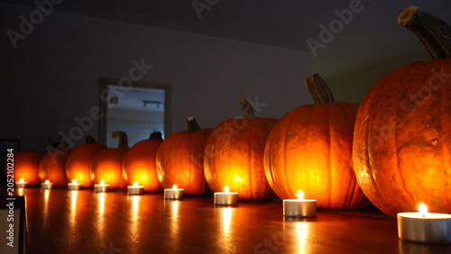 Obraz na plátně Row of brightly lit pumpkins and small tea light candles creating a warm, festiv