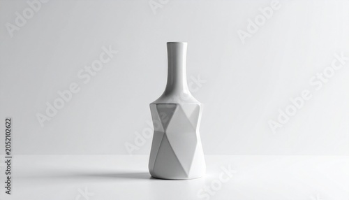 A geometric white vase sits on a table against a plain background