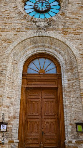Charles's Church presenting its historic wooden entrance door, arched brick facade, and blue stained glass clock window, featuring traditional European architectural details