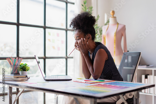 Black woman fashion designer concentrating on work  looking at laptop while brainstorming ideas for new clothing line in creative studio office