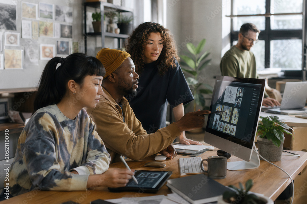 Fototapeta premium Four colleagues collaborate around a large monitor