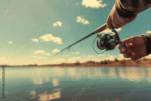 A fishing rod with a spinning reel in the hands of a fisherman on a spring day. Fishing background.