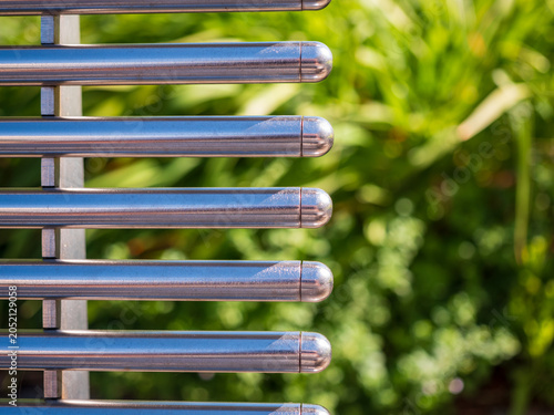 Tableau sur toile Close-up of a modern stainless steel bench backrest with polished tubular bars and soft green background
