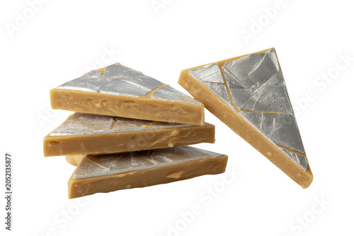Stack of triangular indian kaju katli sweets decorated with thin edible silver leaf foil, arranged on a plain black background, close up