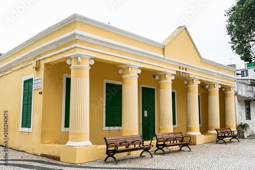 Beautiful yellow facade of historic colonial Coloane Library building built in 1911 with white columns and green wooden shutters in Macau China