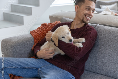 Картината върху платно Mid-adult man in burgundy sweater and jeans cradling golden retriever puppy on s