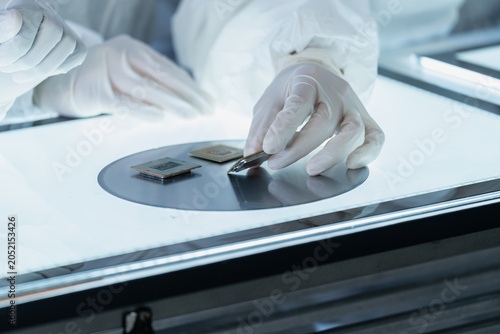 Close-up of a technician's gloved hands carefully inspecting semiconductor microchips and a silicon wafer on an illuminated light table in a cleanroom laboratory.